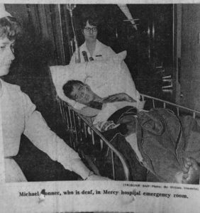 Michael Tonner is shown in a hospital gurney surrounded by two nurses.